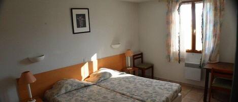 Ein Schlafzimmer mit einem Doppelbett, Nachttischen mit Lampen, einem Fenster mit Vorhängen und einem kleinen Tisch.