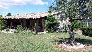 A rustic stone building with a tiled roof, a covered porch, and a well-maintained lawn with a tree and rocks. - Vrbo Property (Grospierres)