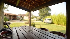 An outdoor wooden table with chairs, a clear view of a grassy area, and a white van in the background. - Vrbo Property (Grospierres)