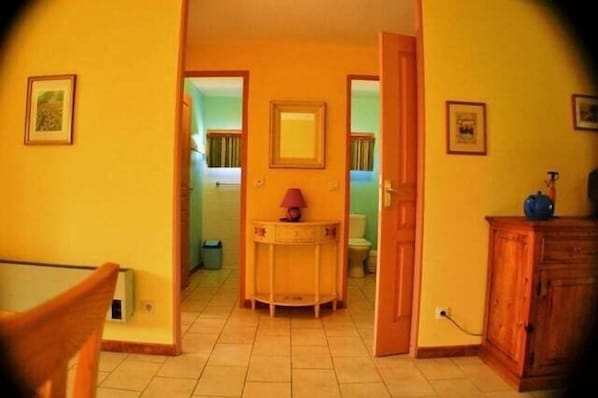 Un passadís amb una porta que dona a un bany, una taula petita amb una làmpada i un armari.