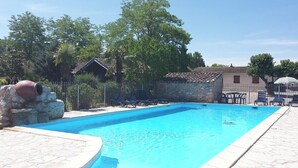 A swimming pool with lounge chairs and a stone wall. - Vrbo Property (Grospierres)