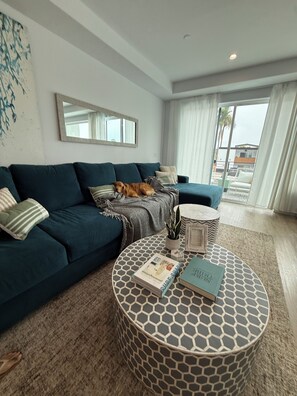 A modern living room with a dark blue sofa, a round coffee table with a geometric pattern, and a large window with curtains. - Beach Haus~Modern Comfort Spacious 4-bedroom in Pacific Beach/La Jolla (San Diego)