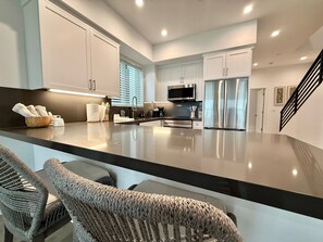 A modern kitchen with white cabinetry, stainless steel appliances, and a black countertop. - Beach Haus~Modern Comfort Spacious 4-bedroom in Pacific Beach/La Jolla (San Diego)