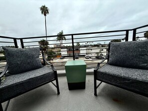 A balcony with two grey upholstered chairs and a green ottoman. - Beach Haus~Modern Comfort Spacious 4-bedroom in Pacific Beach/La Jolla (San Diego)