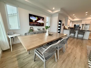 A modern dining area with a long wooden table, wicker chairs, and a flat-screen TV mounted on the wall. - Beach Haus~Modern Comfort Spacious 4-bedroom in Pacific Beach/La Jolla (San Diego)