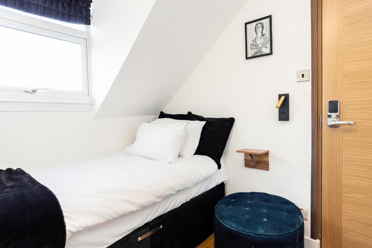 A small, neatly arranged bedroom with a bed, a bedside table, a wall-mounted light, and a door.