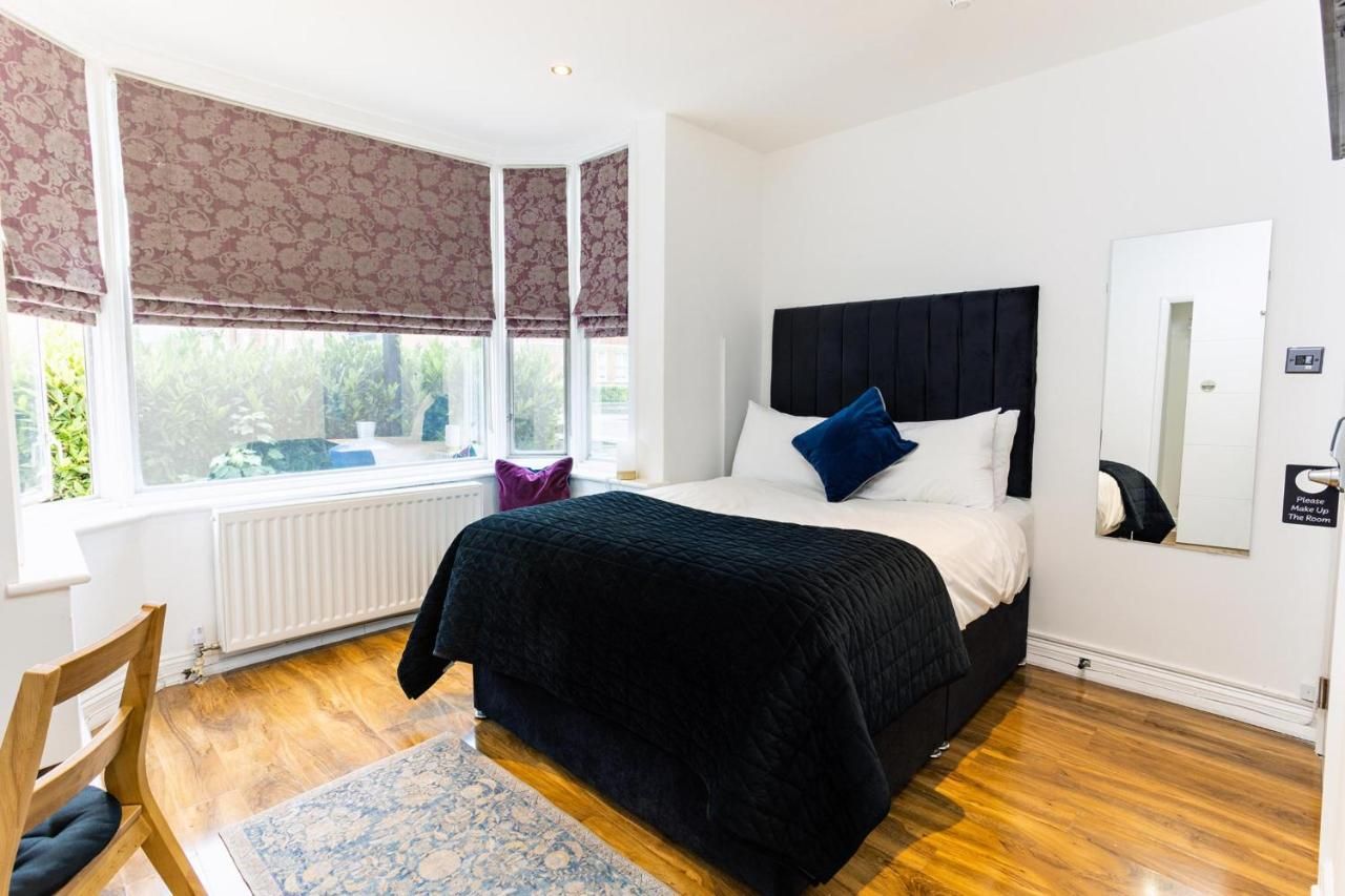 A bedroom with a large bed, a window with curtains, a radiator, a wooden floor, and a chair.