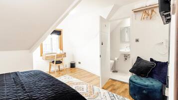 A bedroom with a bed, a desk, and a bathroom with a sink and mirror.