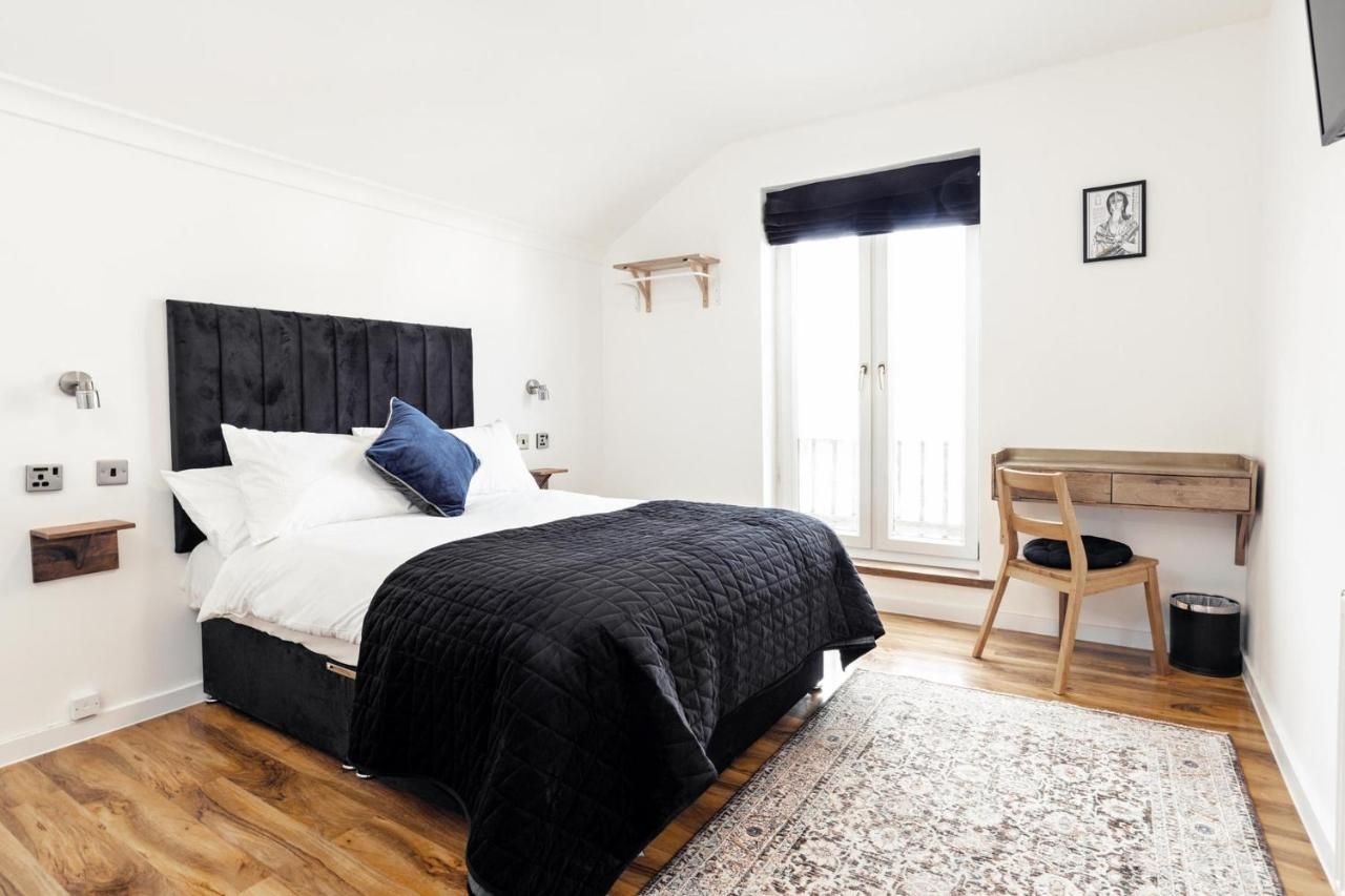 A bedroom with a bed, a desk, a chair, a window, and a small shelf.