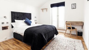 Un dormitorio con cama, escritorio, silla, ventana y una pequeña estantería.