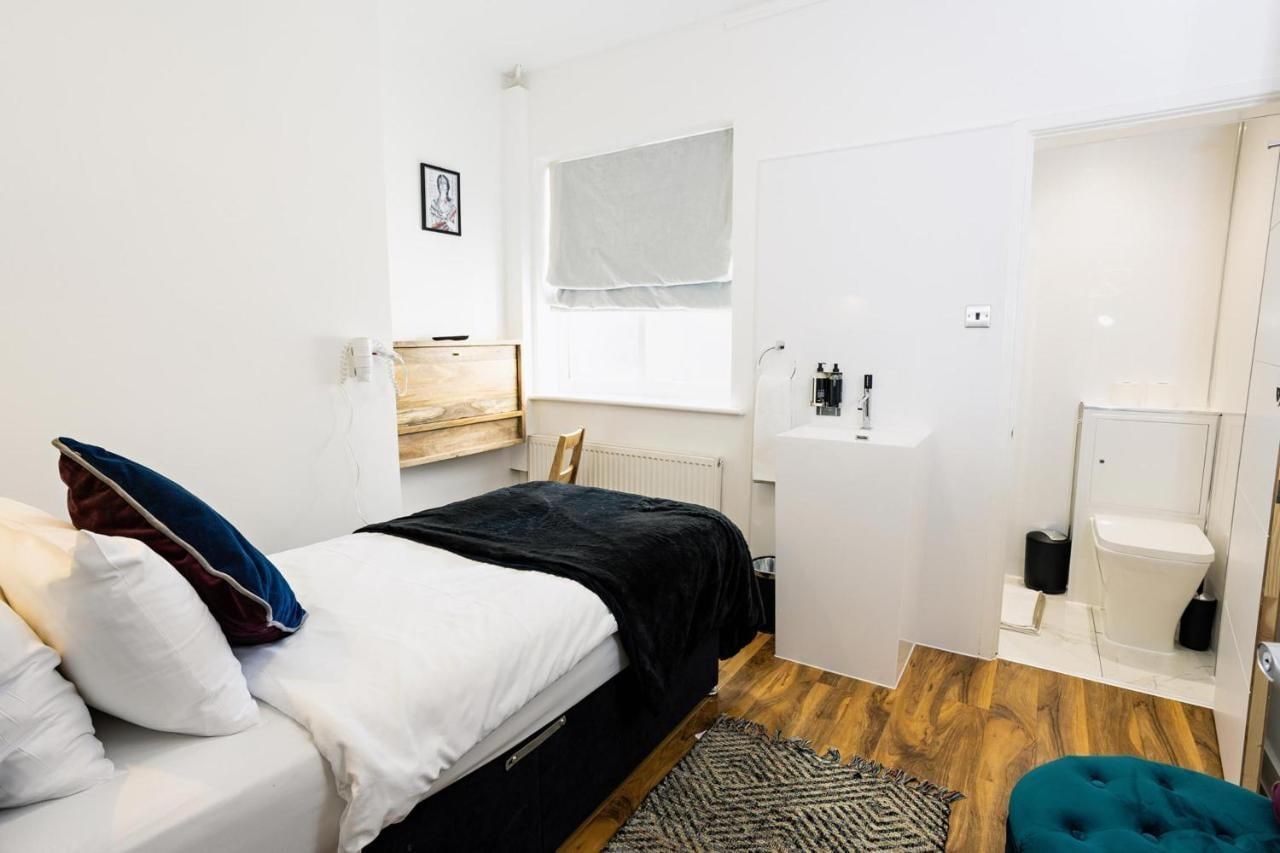 Une chambre à coucher comprenant un lit, une table de chevet, une fenêtre, une armoire intégrée et une salle de bain avec des toilettes et un lavabo.
