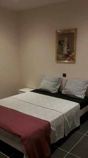 Ein Schlafzimmer mit einem Bett, zwei Kissen, einem Nachttisch, einem gerahmten Bild an der Wand und einer roten Decke.