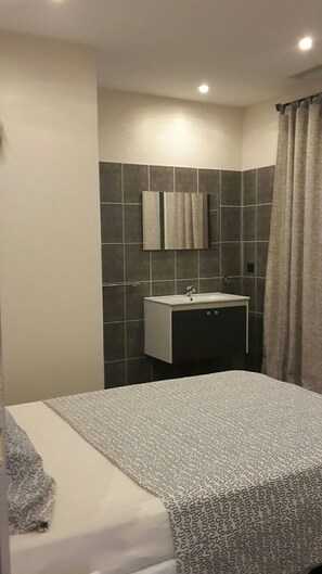 Habitación de hotel con cama, baño con lavabo y espejo, y cortina de ducha.