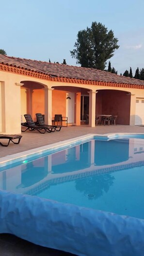 Ein Schwimmbecken mit Liegestühlen und einer überdachten Terrasse.