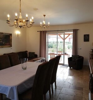 A dining area with a table set for four, a chandelier, and a view through a glass door to an outdoor patio. - "Chez Nous" Villa, with Air Conditioning, Pool, BBQ, and Terrace (Grospierres)