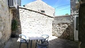 A stone wall with a small window, a table with chairs, and a potted plant. - Vrbo Property (Grospierres)