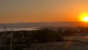Pôr do sol sobre uma paisagem costeira com edifícios e estrada.