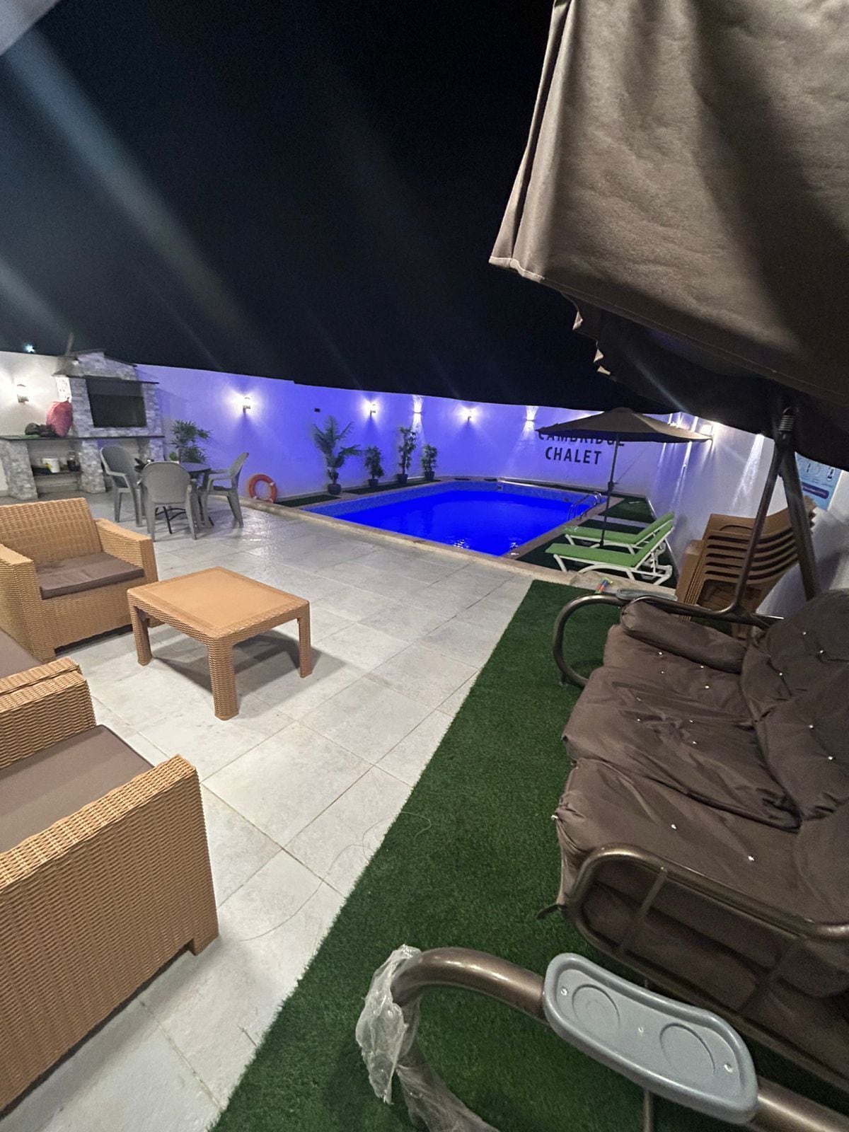 En uteplats med pool, sittgrupp och en överbyggd grillplats.