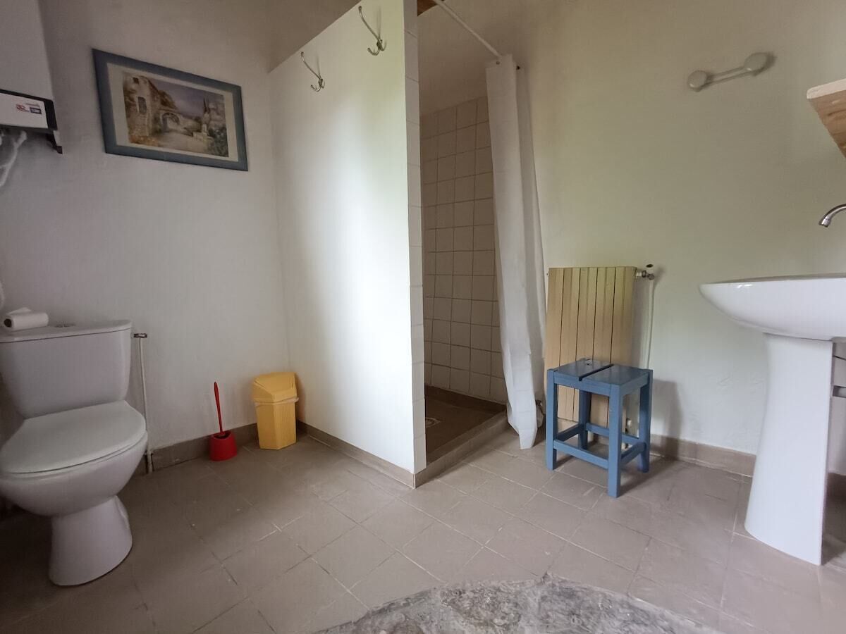 Un baño con inodoro, lavamanos, ducha y un taburete pequeño.
