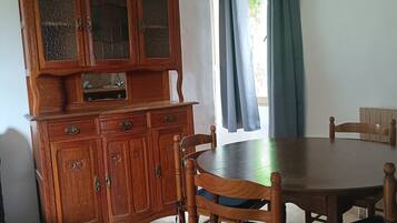 Un comedor con una mesa y sillas de madera, un aparador con puertas de vidrio y una ventana con cortinas.