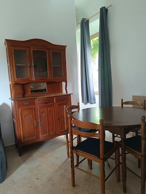 A dining area with a wooden table and chairs, a cabinet with glass doors, and a window with curtains. - Vacation Rental #7, Sleeps 2, Domaine de Ribiere (Grospierres)