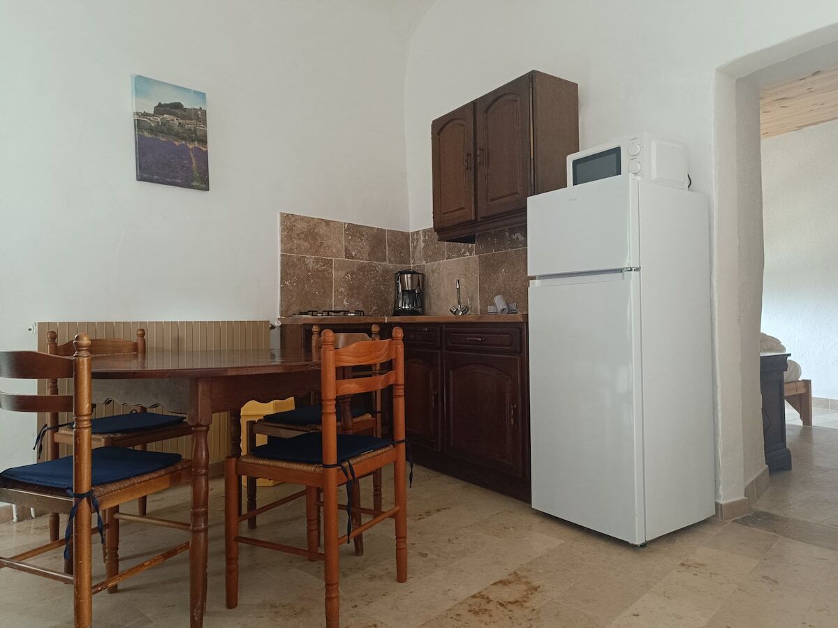 Cocina compacta con una mesa y sillas, un refrigerador blanco y armarios de madera oscura.