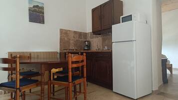 Cocina compacta con una mesa y sillas, un refrigerador blanco y armarios de madera oscura.