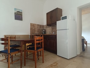 A compact kitchen with a dining table and chairs, a white refrigerator, and dark wooden cabinets. - Vacation Rental #7, Sleeps 2, Domaine de Ribiere (Grospierres)