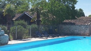 A swimming pool with lounge chairs and a stone wall. - Vrbo Property (Grospierres)