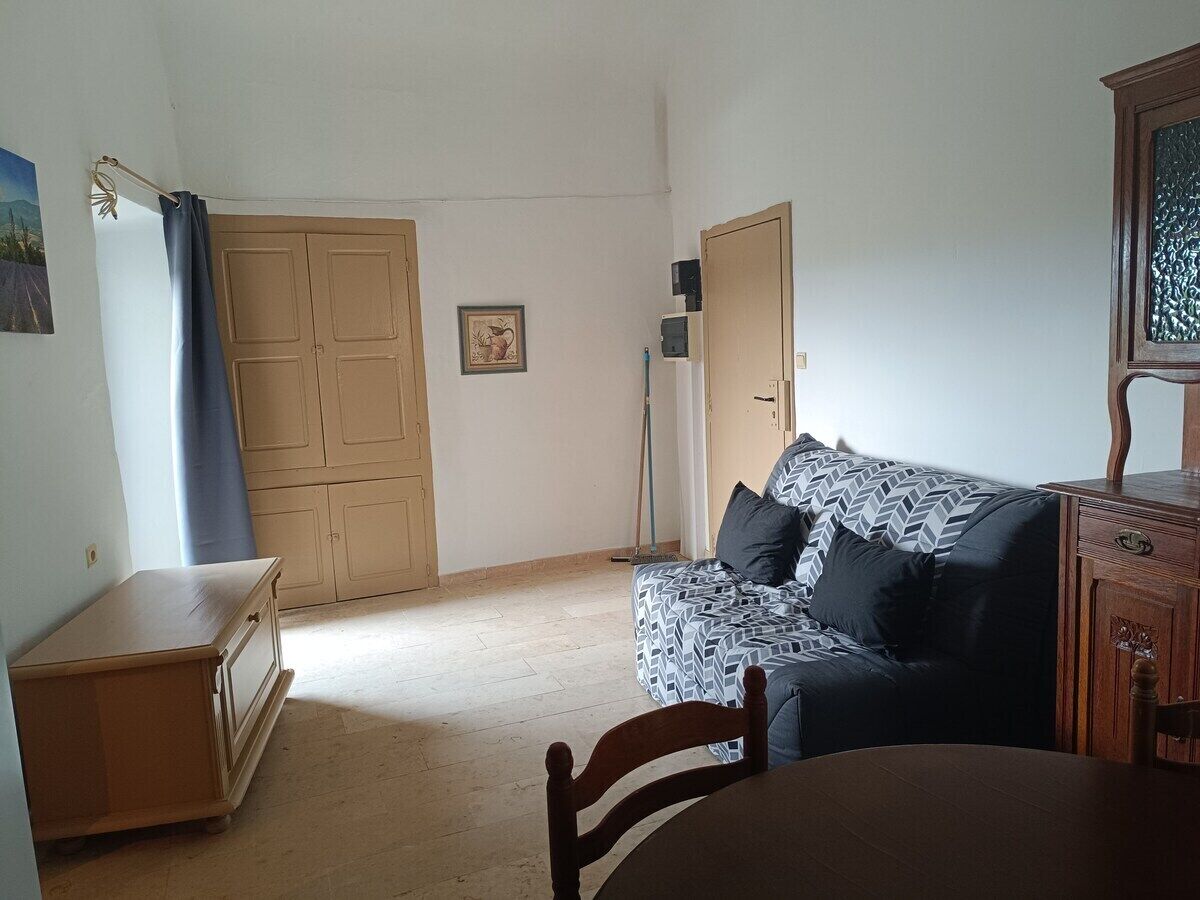 Een kamer met een houten kast, een bank met gestreepte kussens, een eettafel en een gesloten deur.