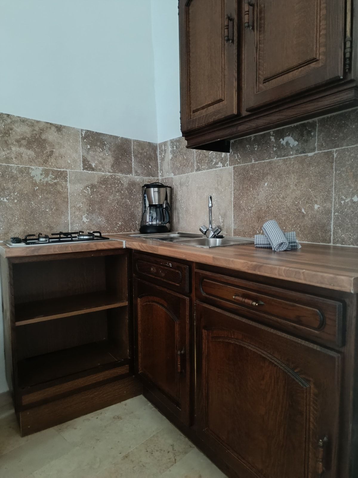 Een keuken met een gasfornuis, een koffiezetapparaat en houten kasten.