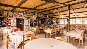 A restaurant with wooden beams, tables with white tablecloths, and various posters on the walls. - Vrbo Property (Grospierres)