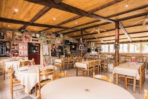 Ein Restaurant mit Holzbalken, Tischen mit weißen Tischdecken und verschiedenen Postern an den Wänden.