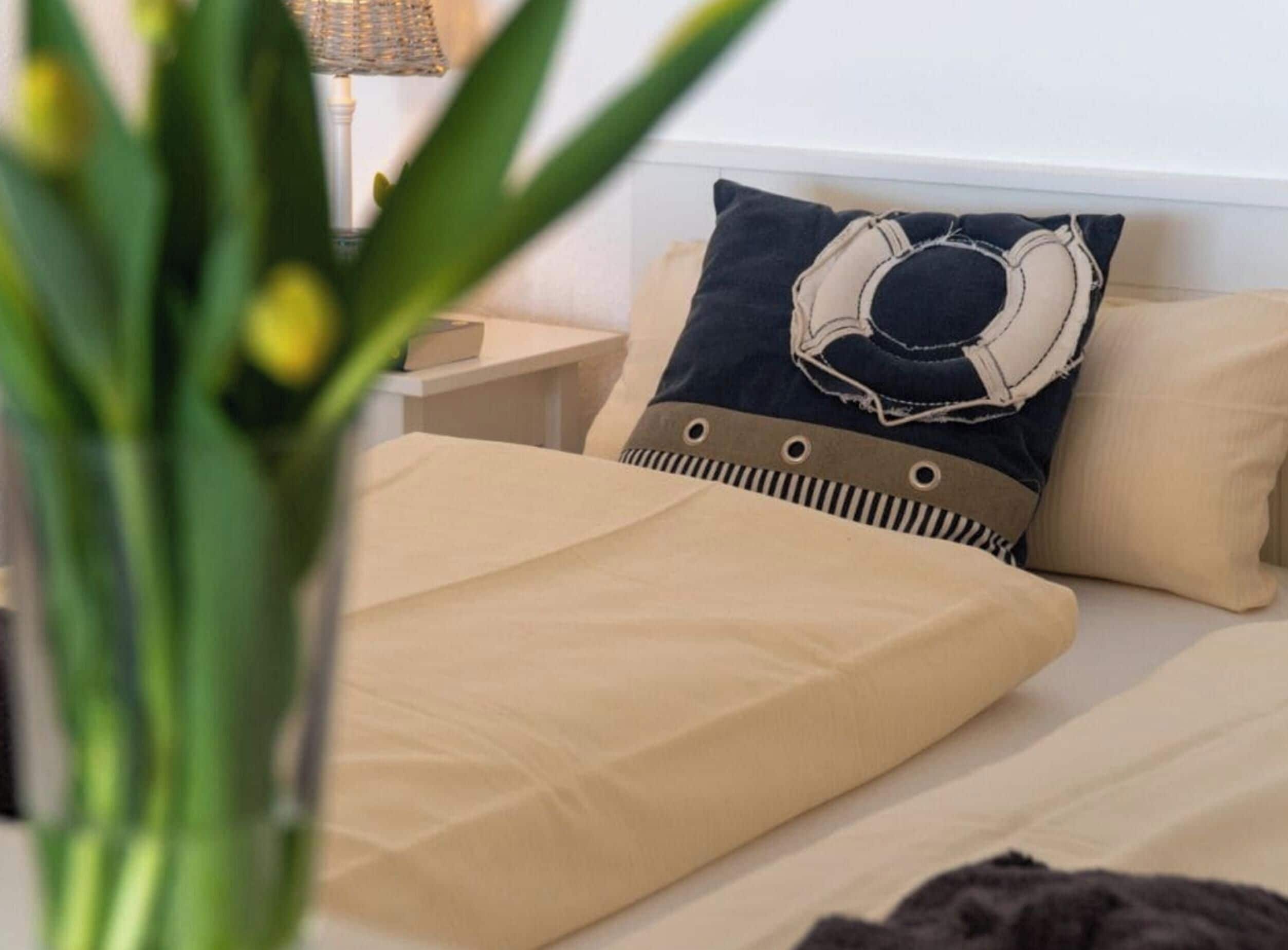 Una cama con ropa de cama color beige, una almohada con diseño vaquero y una mesita de noche con una lámpara.