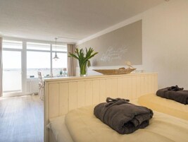 A hotel room with a large window, a bedside table with a decorative bowl, and two beds with towels.