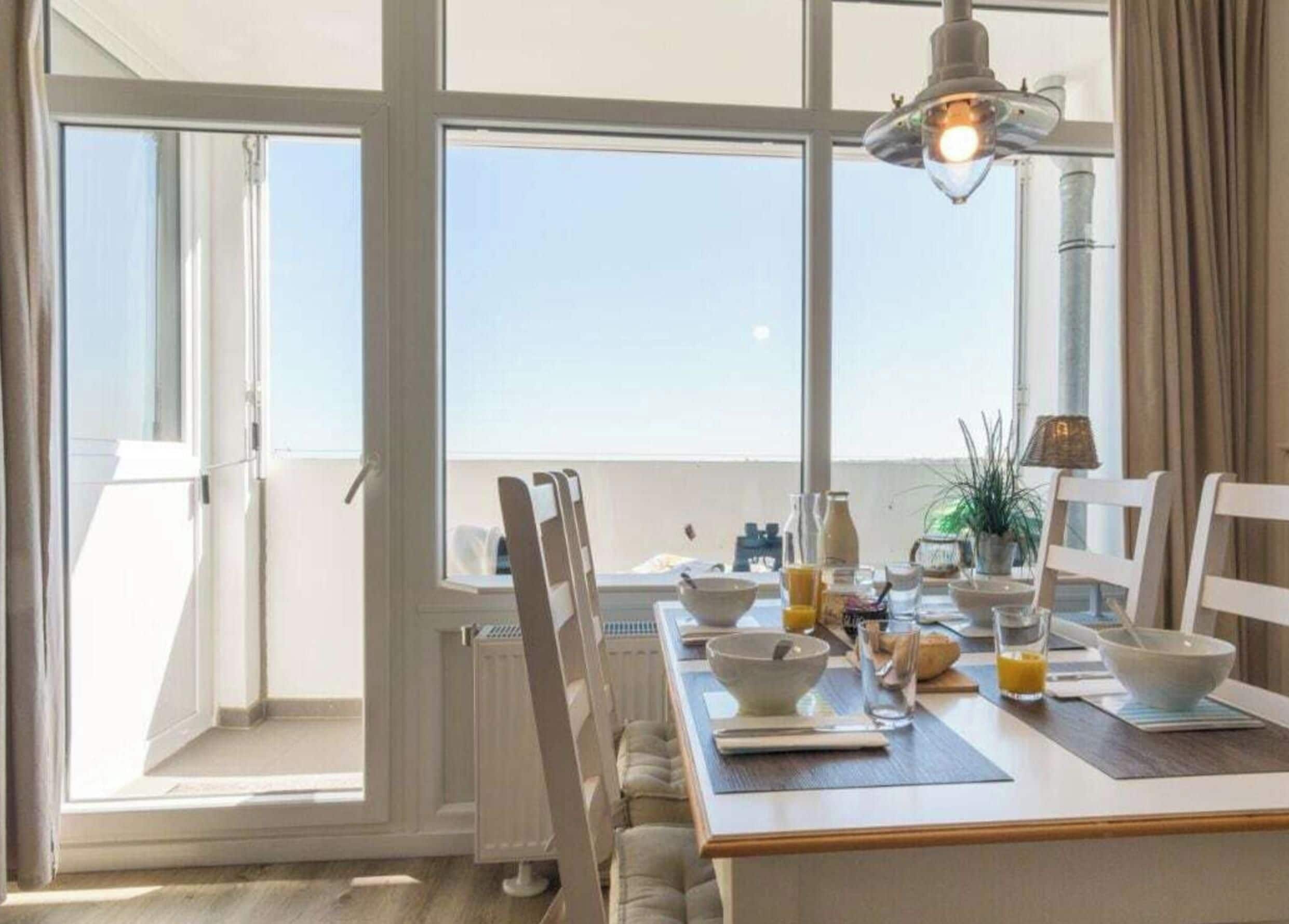 A dining area with a table set for two, a window with curtains, and a view of the sky.