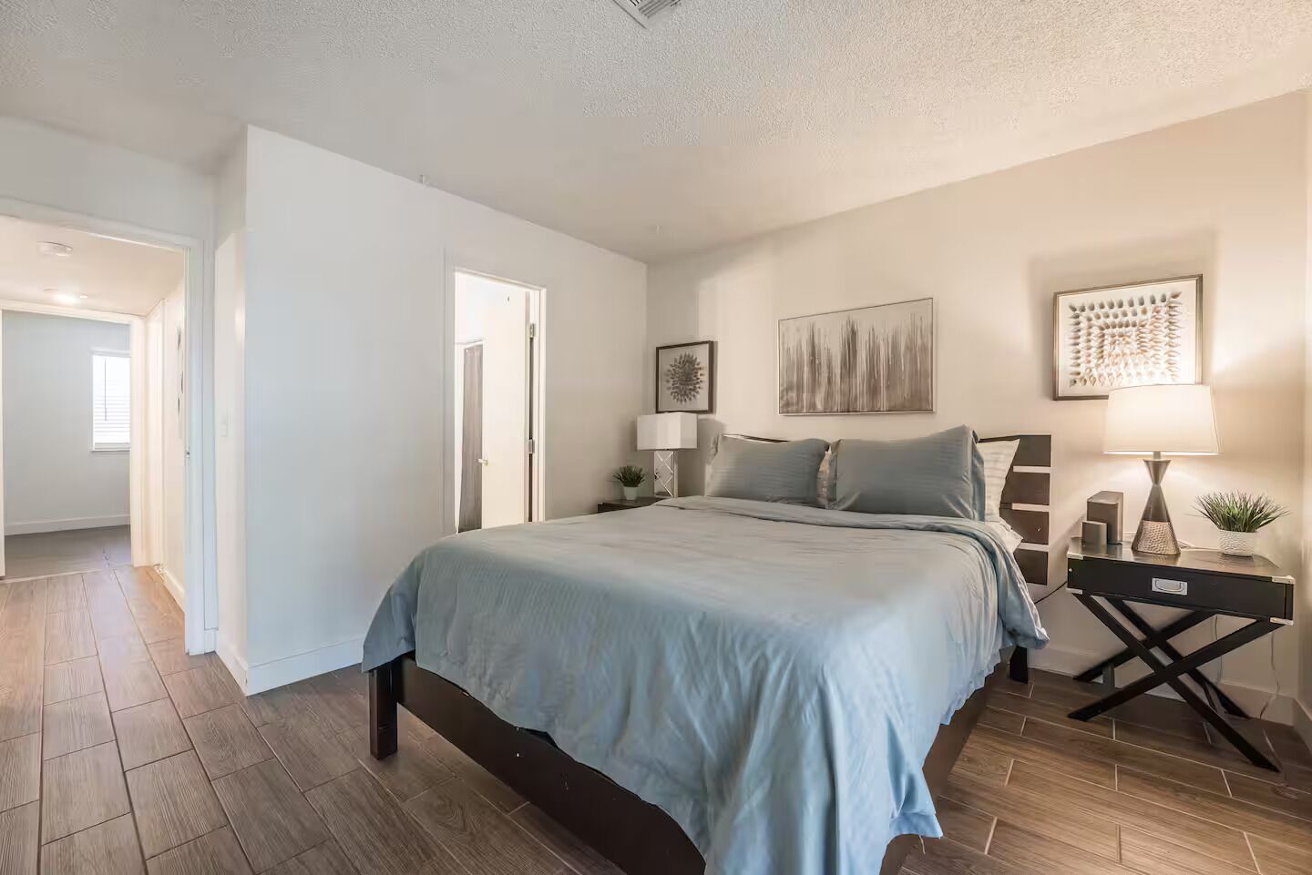A bedroom with a bed, bedside tables, a nightstand, and a door leading to another room.