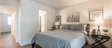 A bedroom with a bed, bedside tables, a nightstand, and a door leading to another room.