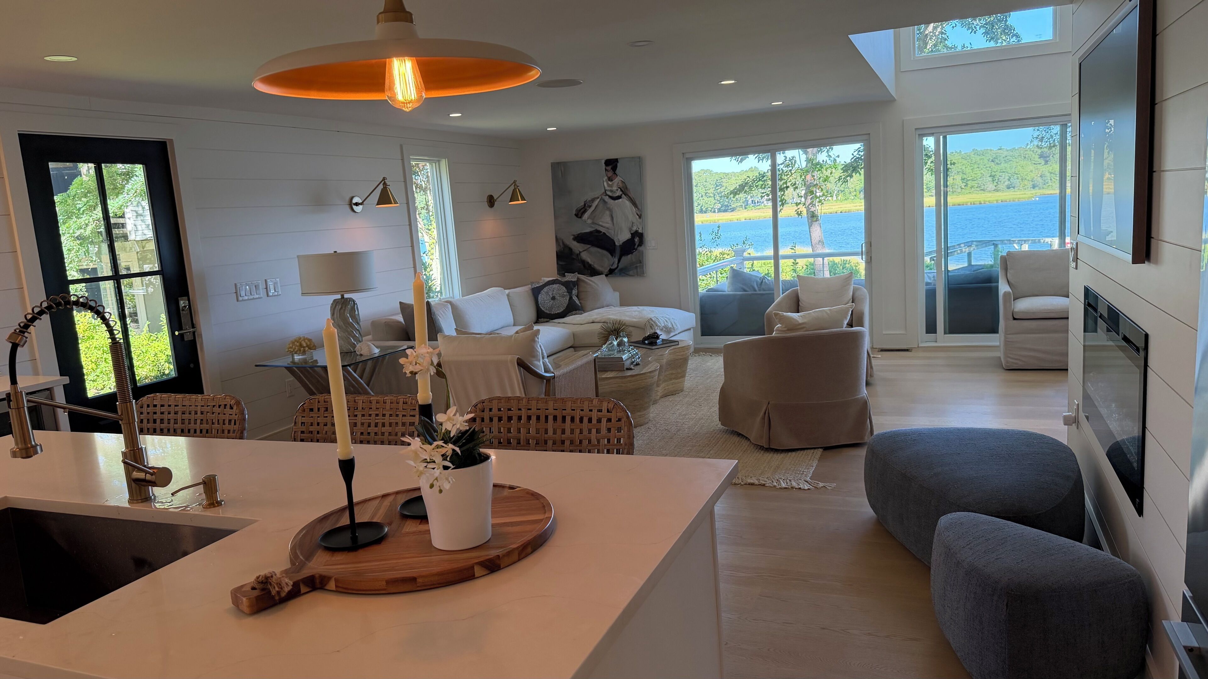 A modern living room with a large window, a dining area with a central island, and a view of a lake.