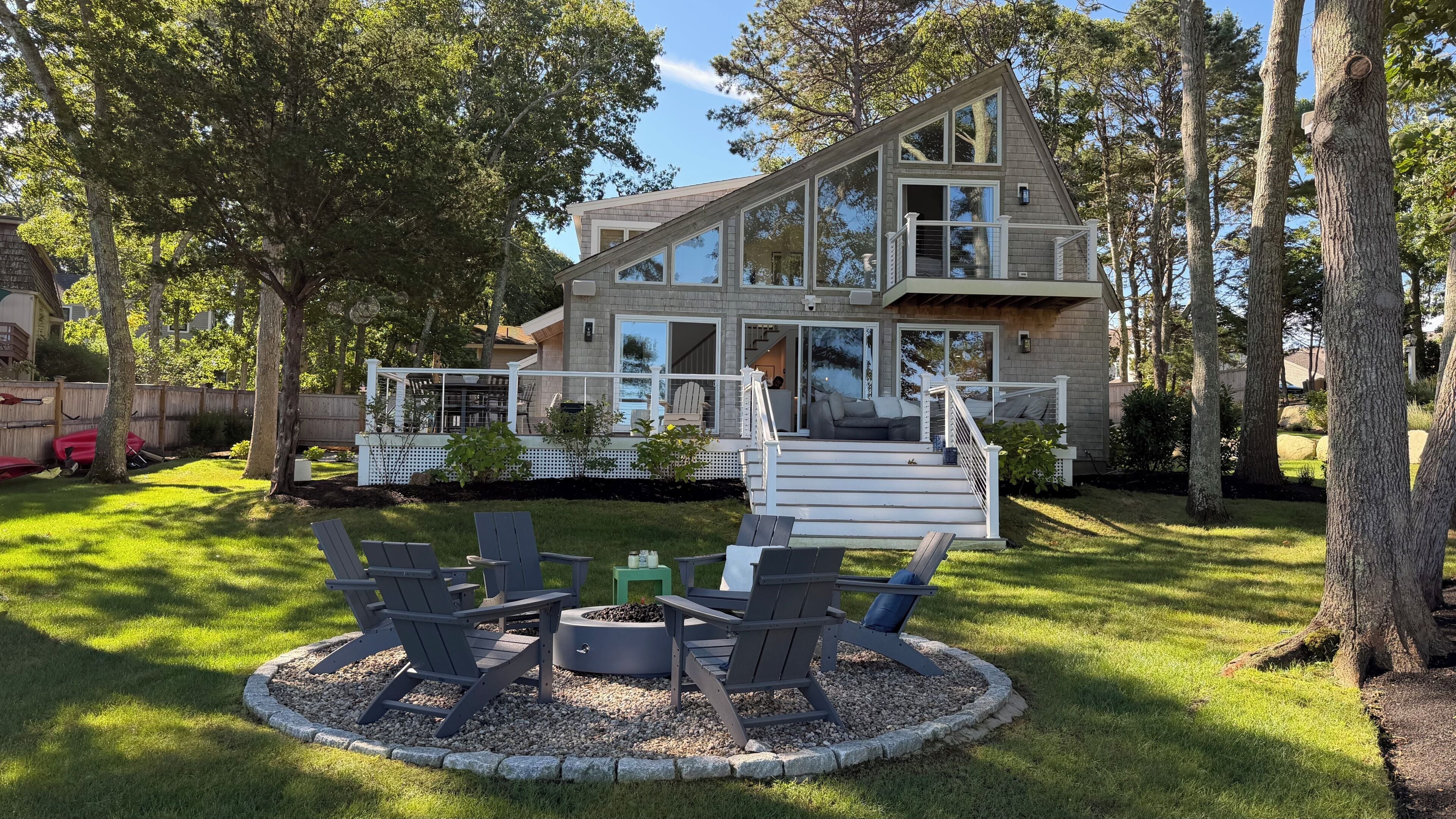 A modern two-story house with a deck, outdoor seating, and a fire pit.