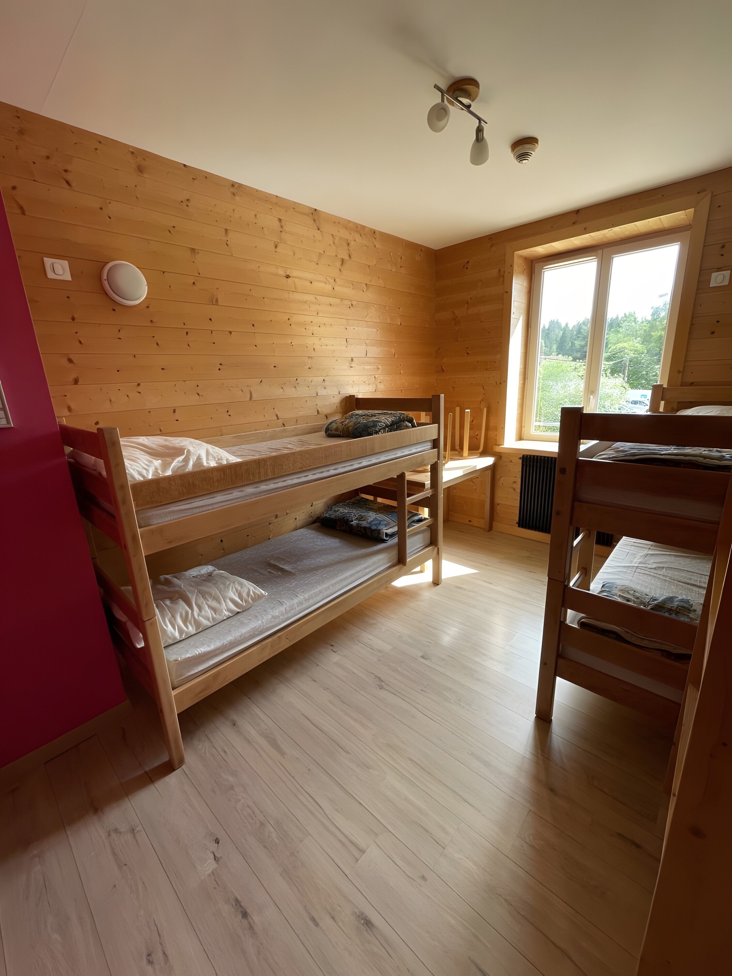 A room with wooden bunk beds, a window with a view, and a ceiling fan.