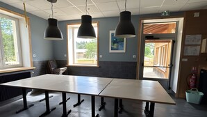 A conference room with a long table, three pendant lights, and a view through a door to an outdoor area.