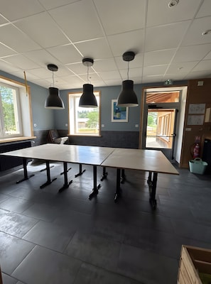 A conference room with a long table, three pendant lights, and a view through a door to an outdoor area.