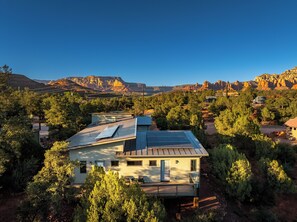 Uma casa moderna com painéis solares, rodeada por árvores e montanhas.