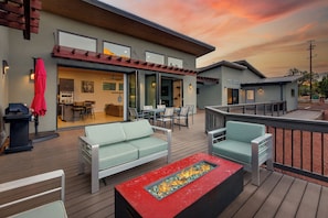Um terraço moderno ao ar livre com assentos, lareira e vista da propriedade.