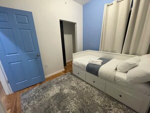 Een slaapkamer met een bed, een deur, een kleine kast en een badkamedeur.