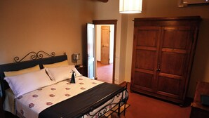 A bedroom with a bed, a nightstand, a lamp, and a wardrobe. - Vrbo Property (Toscana)