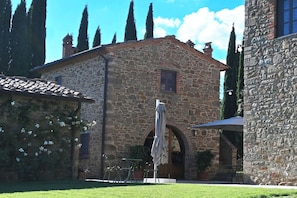 A stone building with a tiled roof, an arched doorway, and a small window. There are outdoor tables and chairs, and a potted plant. - Private Tuscan Estate Surrounded by Vineyards (Toscana)