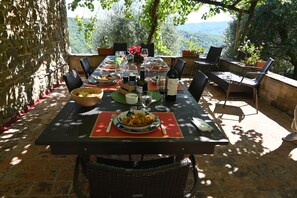 Ein Essbereich im Freien mit Steinmauern, einem Tisch gedeckt mit Tellern, Gläsern und einer Weinflasche.