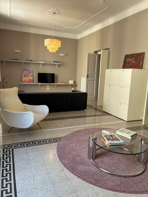 Un salon moderne avec un canapé, une table basse en verre sur laquelle sont posés des livres, un téléviseur et un tapis décoratif.
